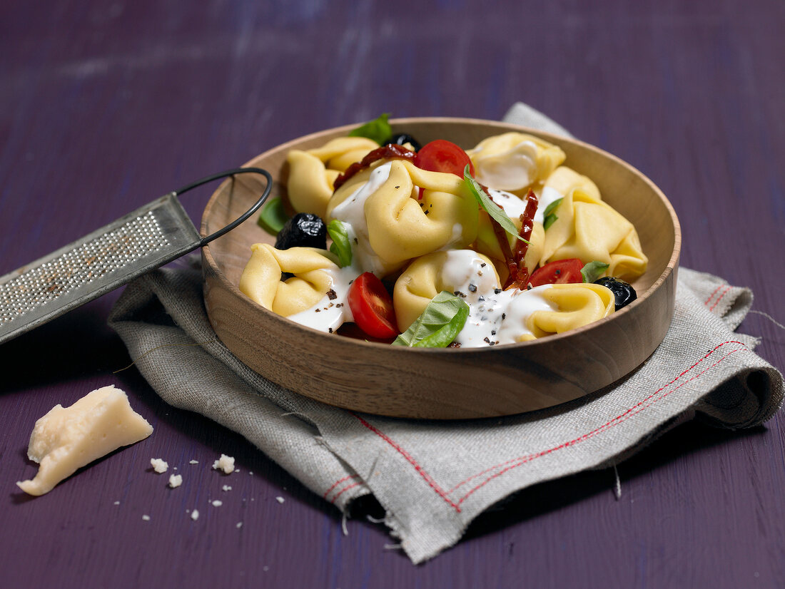 Tortellini salad on wooden plate with grater