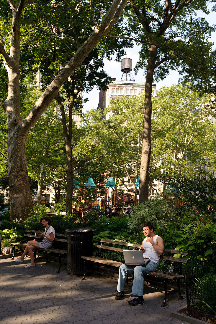 People relaxing in Madison Square Park overlooking skyscrapers, New York, USA