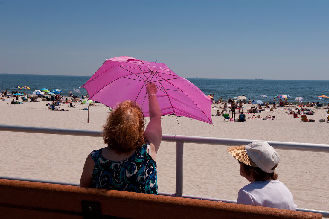 Woman sitting with child and opening umbrella at Long Beach Island, New York, USA
