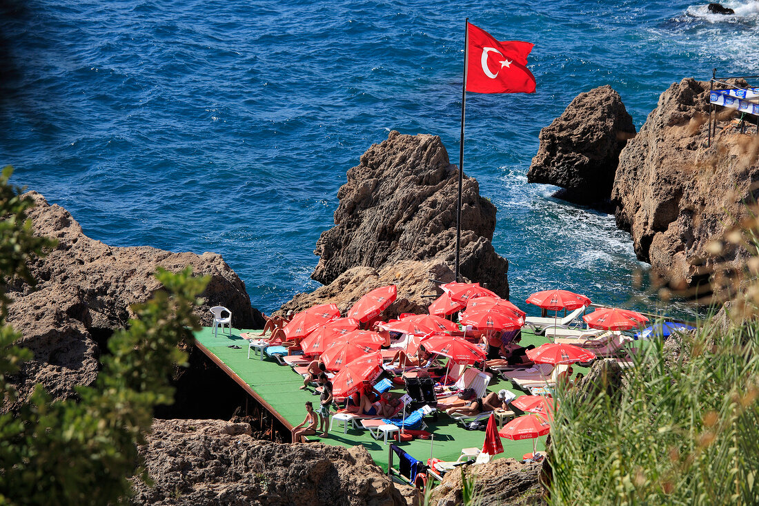 Turkish flag and people relaxing on sun loungers near sea in Antalya, Turkey