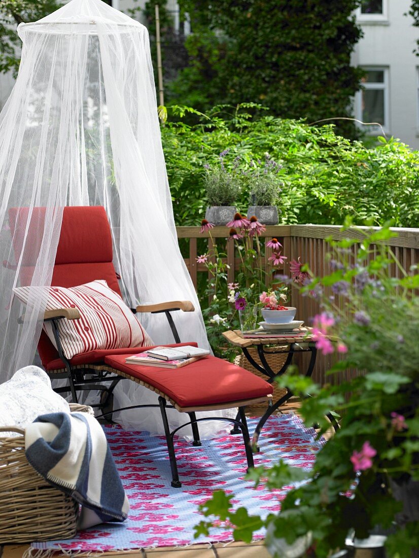 Balcony with red lounger, mosquito net, side table and flowers