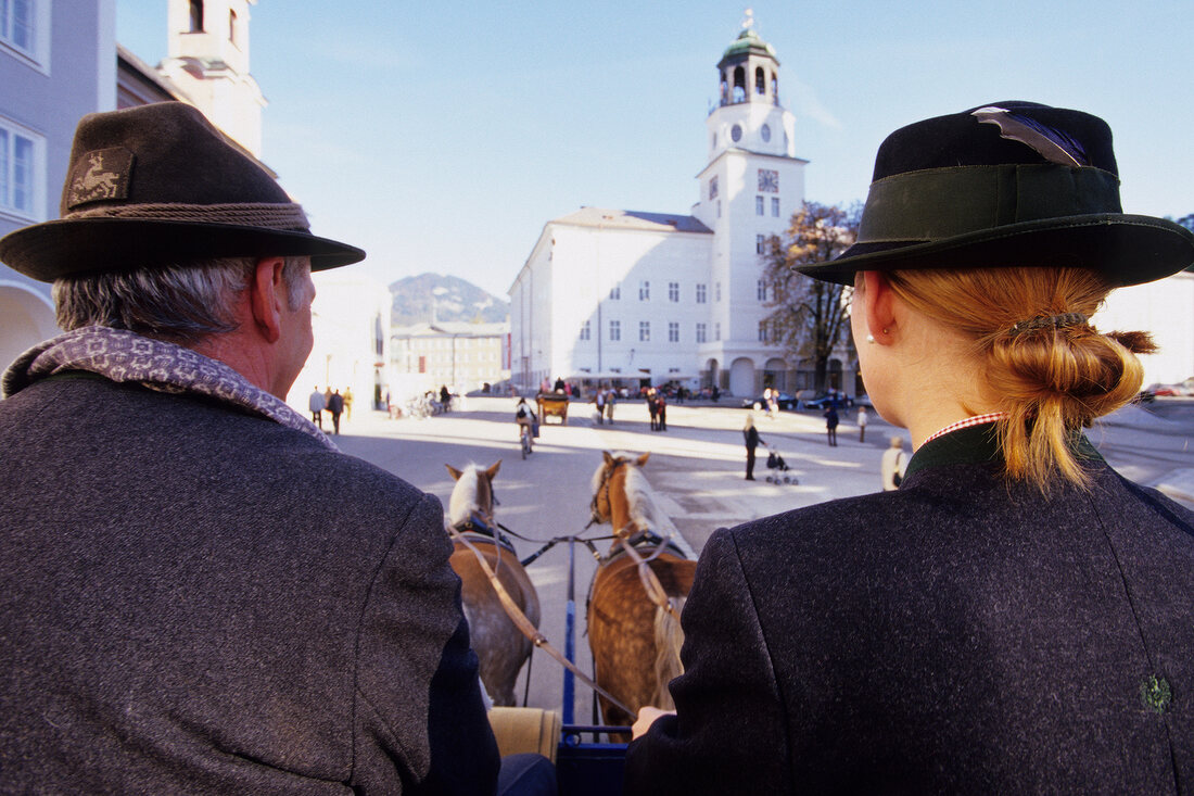 Rear view of two man and woman sitting in horse cab, Salzburg, Austria