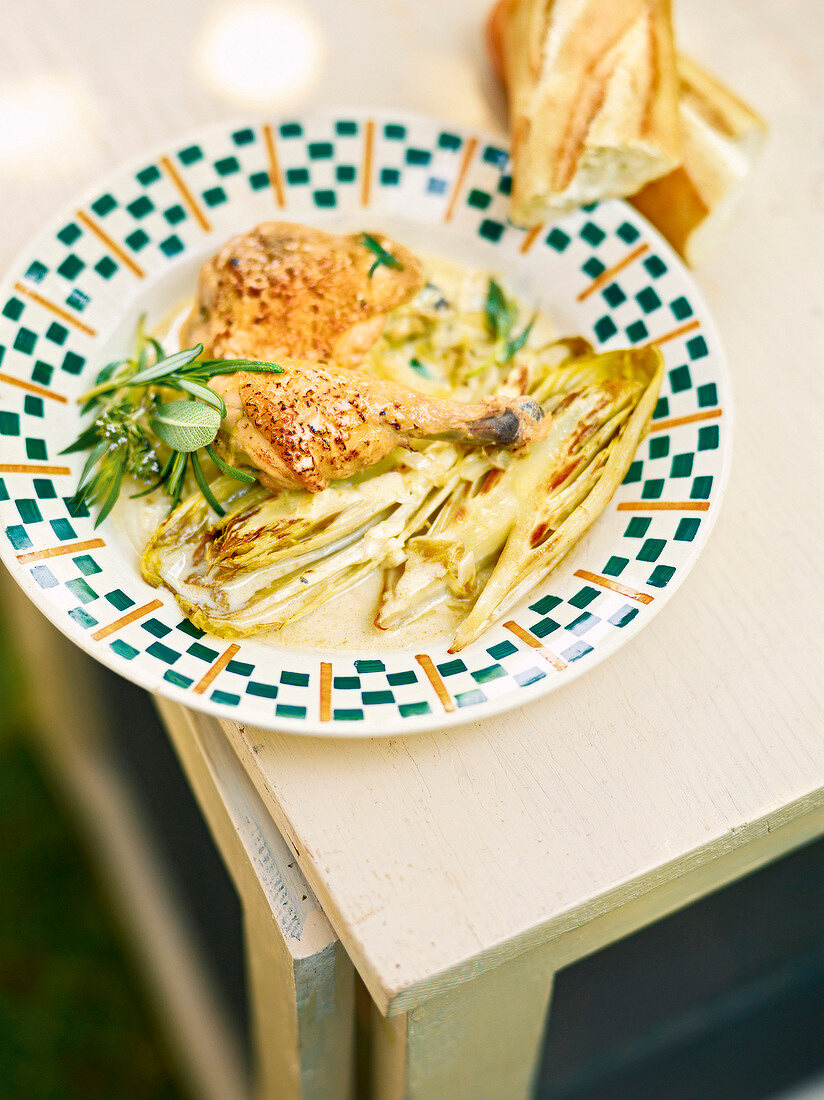 Chicken in wine sauce with chicory on plate, France