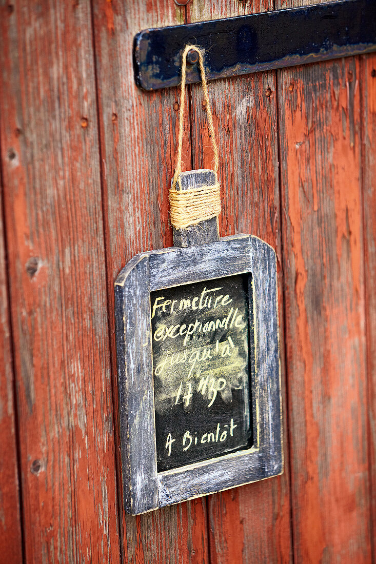 Signboard with opening times on it hanging on wooden wall, France