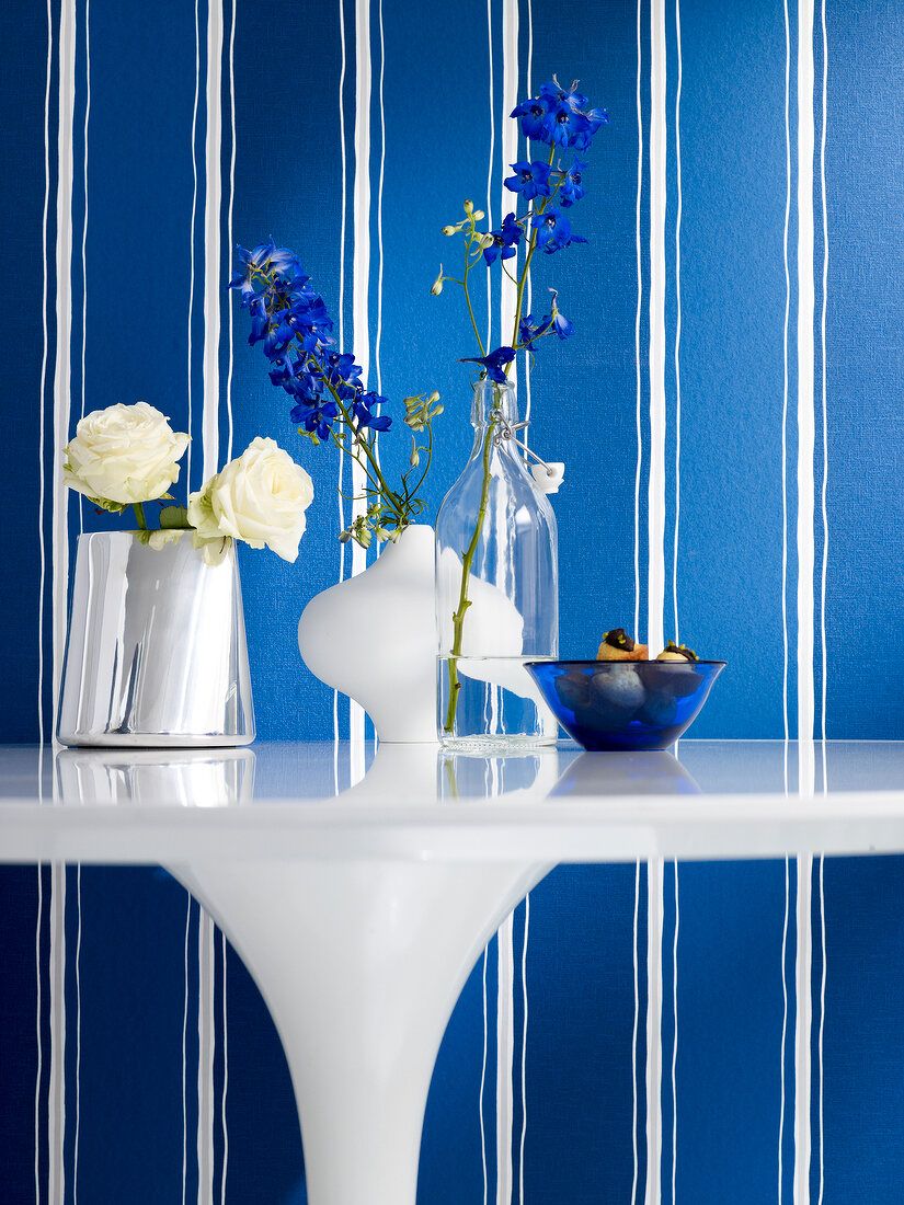 Flower vases on white table against blue and white stripes wallpaper