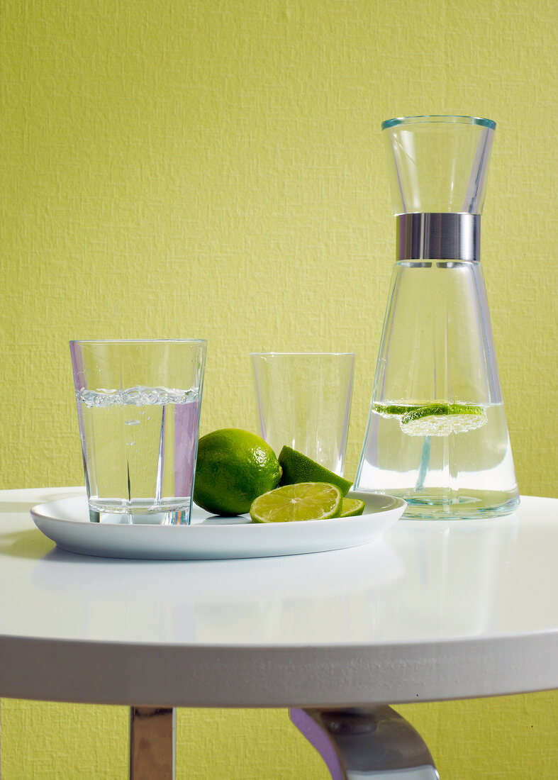 Table with glasses, water bottle and lime against green wall