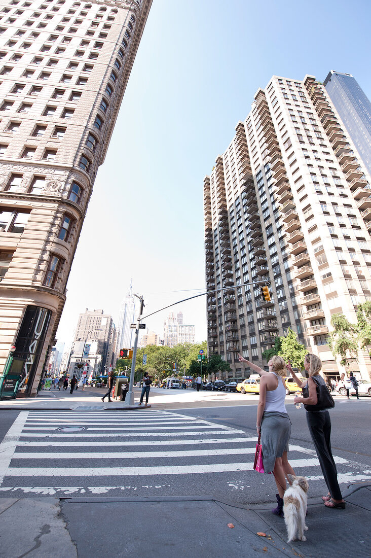 Two women standing on street and pointing up at Flatiron building, New York, USA