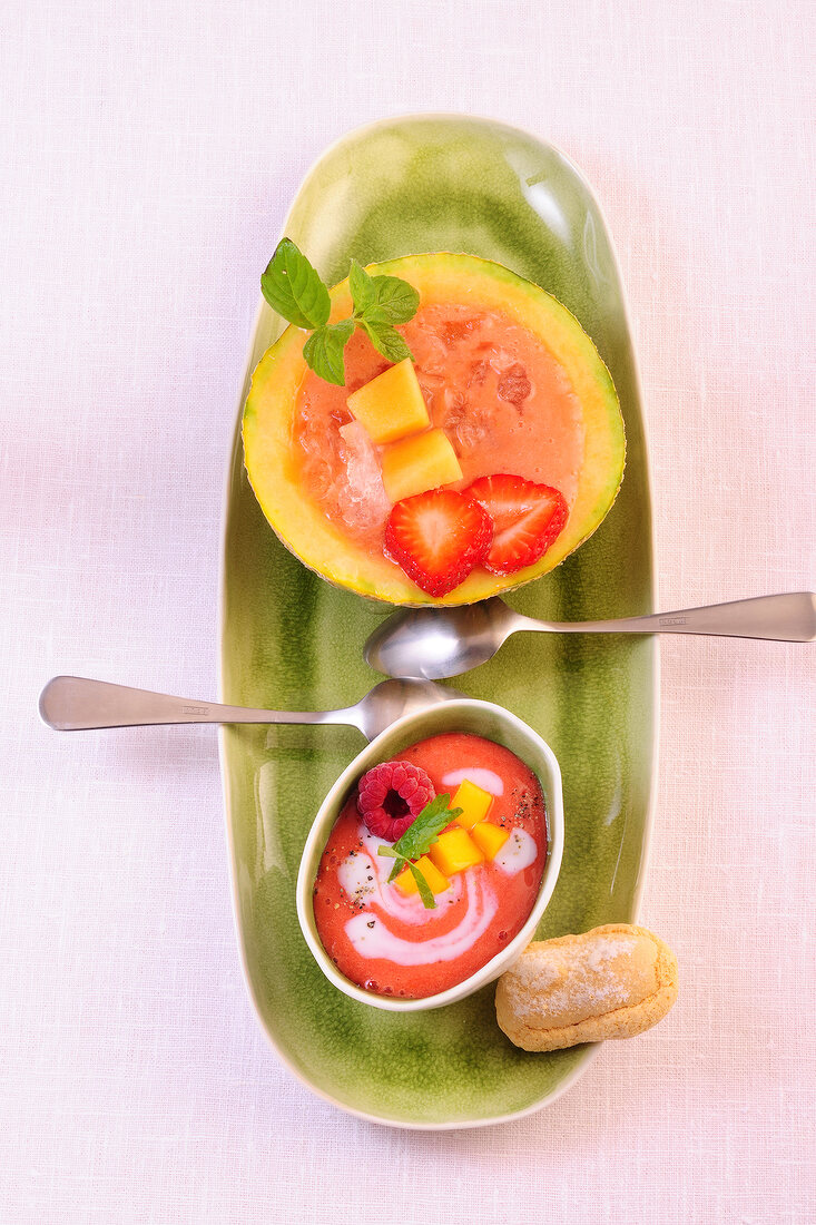 Bowl of strawberry and melon gazpacho with melon and strawberry on tray, overhead view