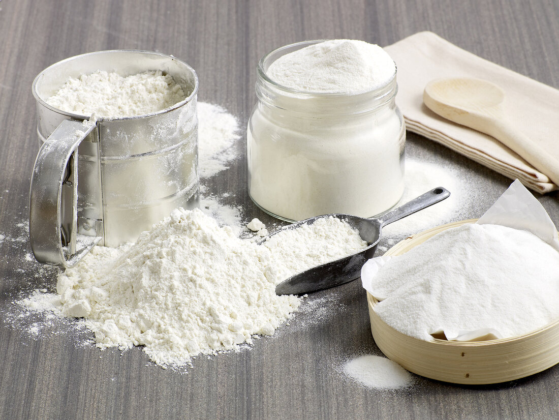 Different types of flours in jar and on wooden board