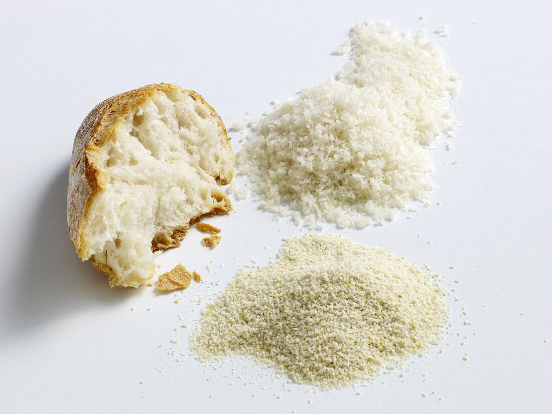 Bread crumbs and piece of bread on white background