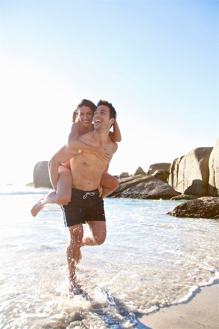 Paar am Strand, beide lachen haben Spaß, laufen durchs Wasser