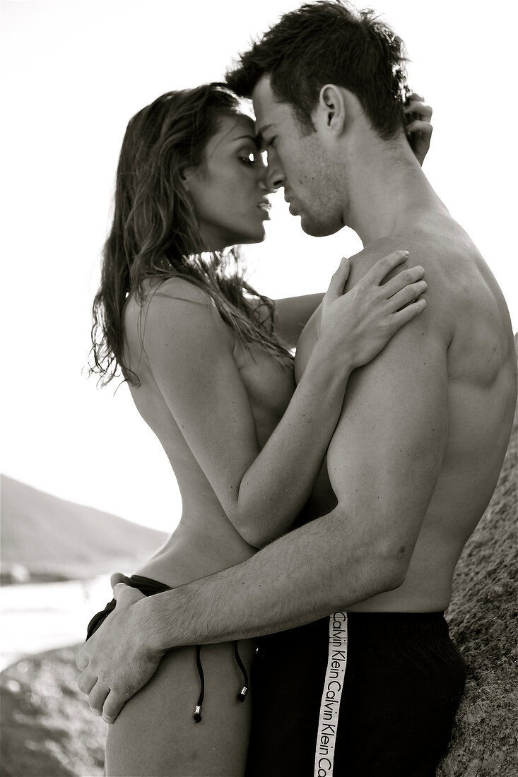Seductive couple embracing each other and leaning against rock, black and white