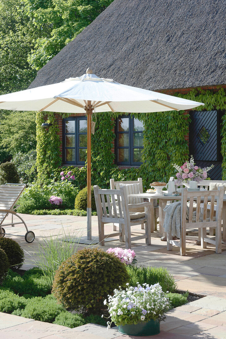 Dining table under parasol against house with wild wine on wall