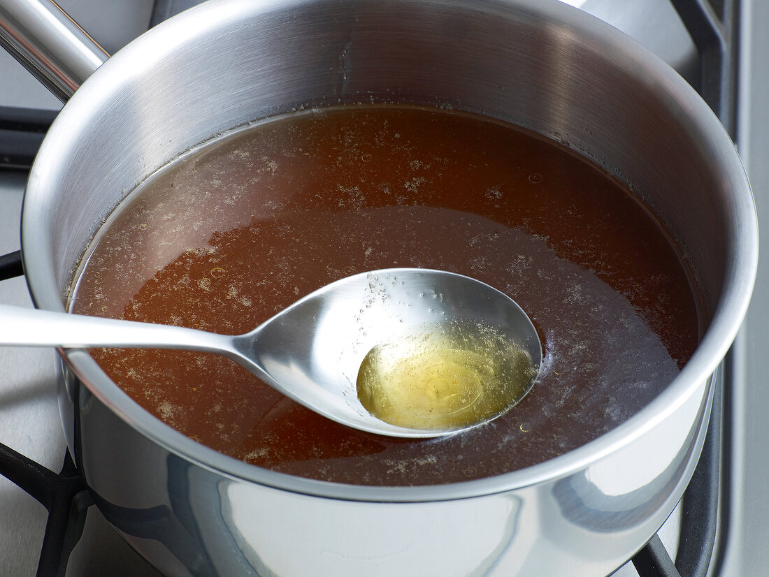 Removing oil by spoon from boiled liquid in pan for preparation of sauce, method 1