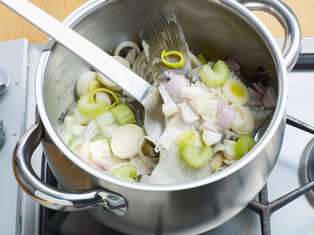 Adding vegetables in pan with fish for preparation of fish stock, step 3