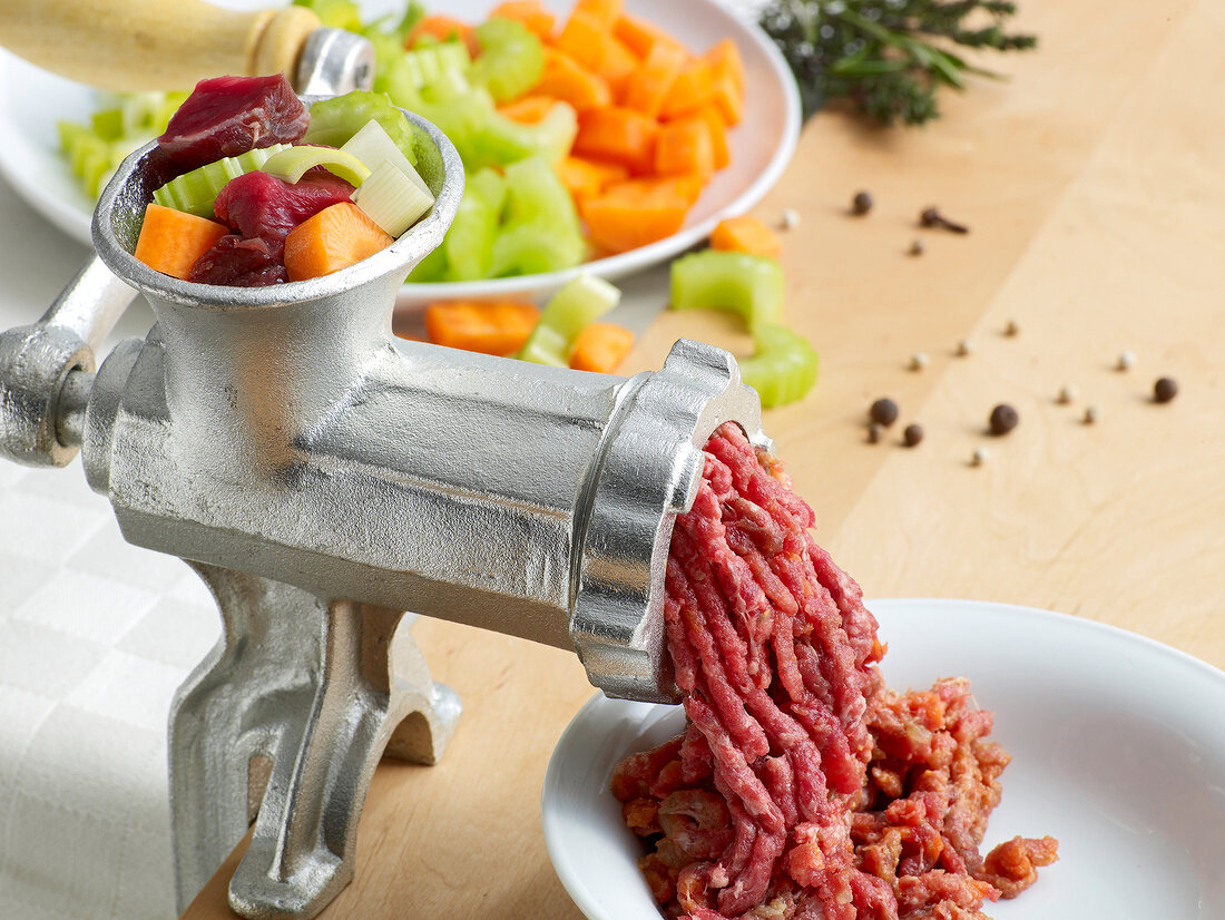 Close-up of vegetables being shredded in shredder for preparation of tomato soup, step 1