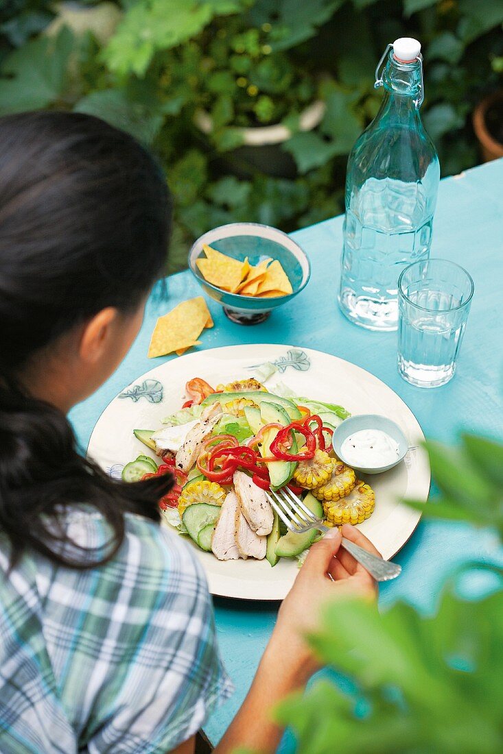 A woman eating and Mexican salad with sweetcorn and chicken breast fillets