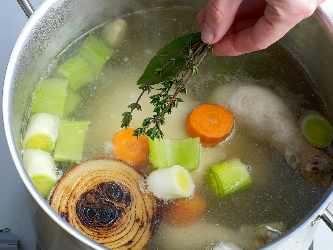 Adding various herbs in pan for preparation of chicken stock, step 4