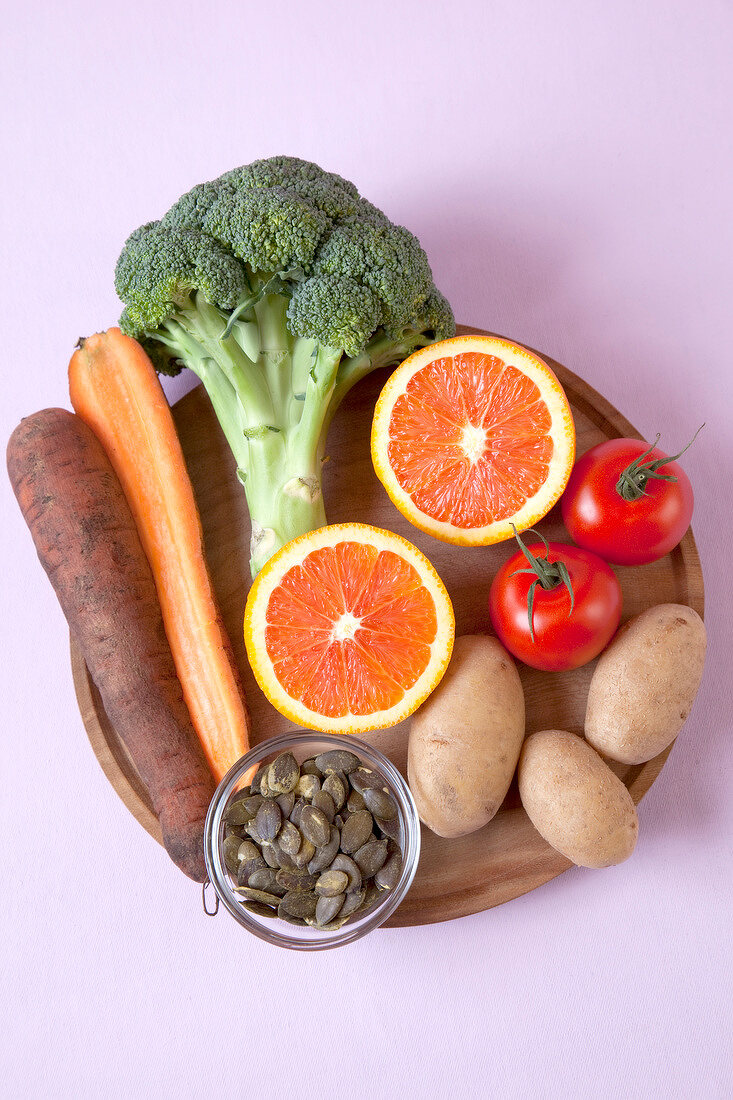 Halved oranges, carrots, tomatoes, potatoes and broccoli on wooden platter