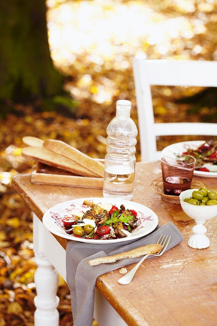 A mixed leaf salad with oyster mushrooms, olives and tomatoes on a table outside