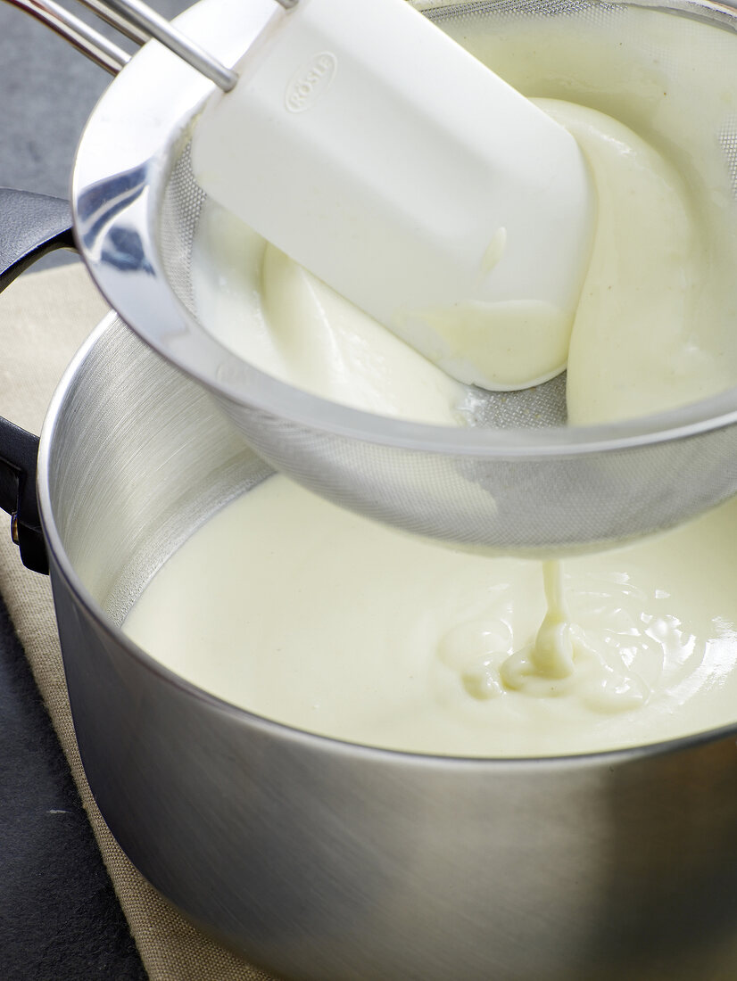 Close-up of mixture being strained through sieve for preparation of bechamel sauce, step 5