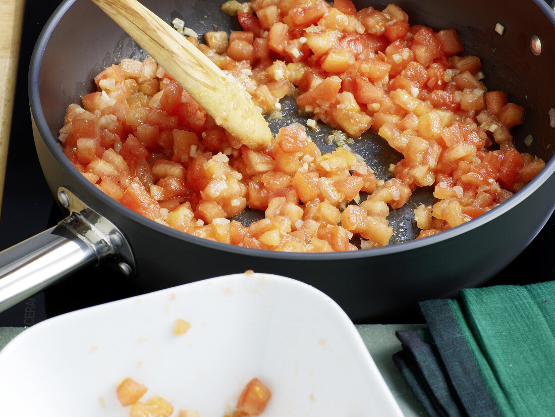 Close-up of chopped tomato being mixed in pan for preparation of tomato concasse, step 3