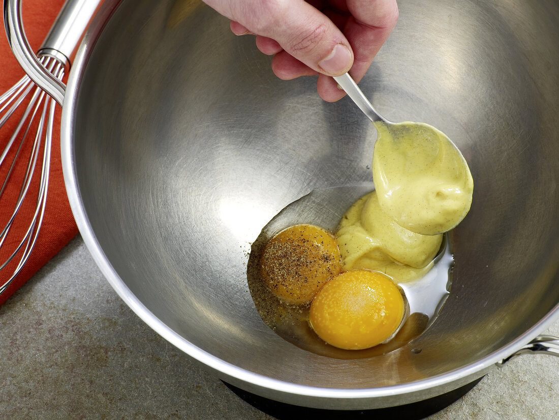 Close-up of mayonnaise being added to egg yolks in wok, step 1