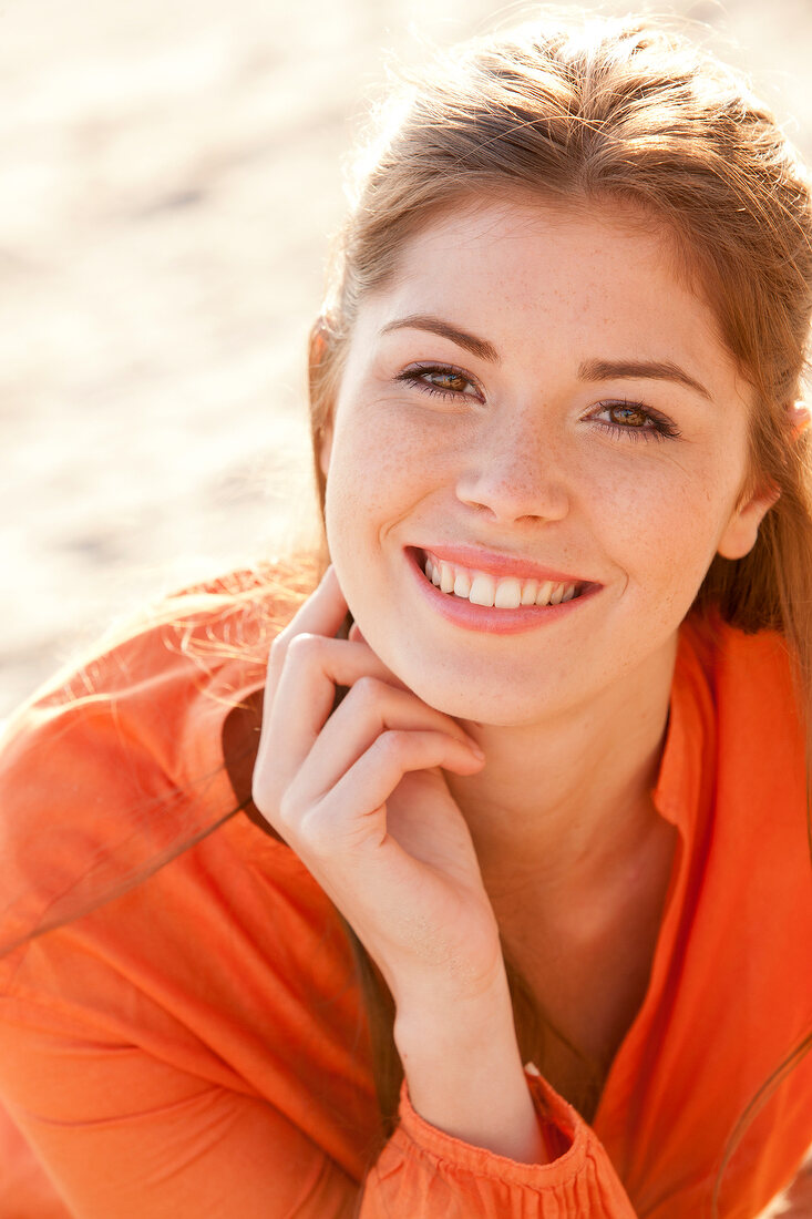 Portrait of pretty brunette woman wearing orange blouse with hand on chin, smiling