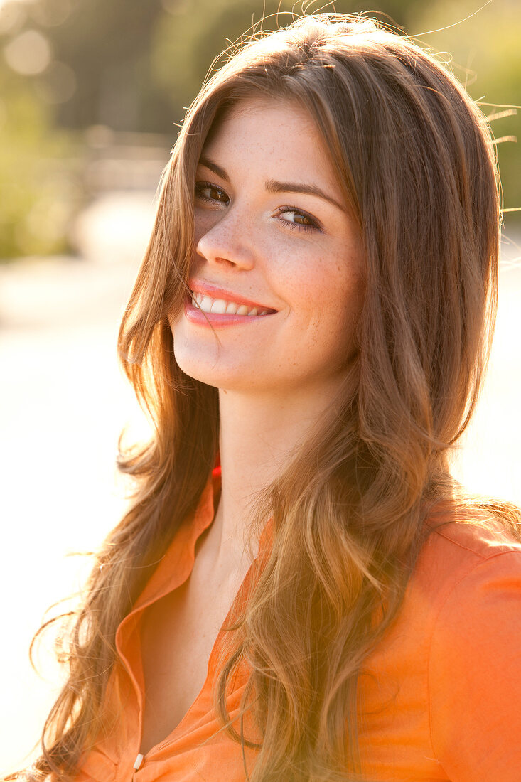 Portrait of happy woman with long brown hair wearing orange blouse, smiling widely