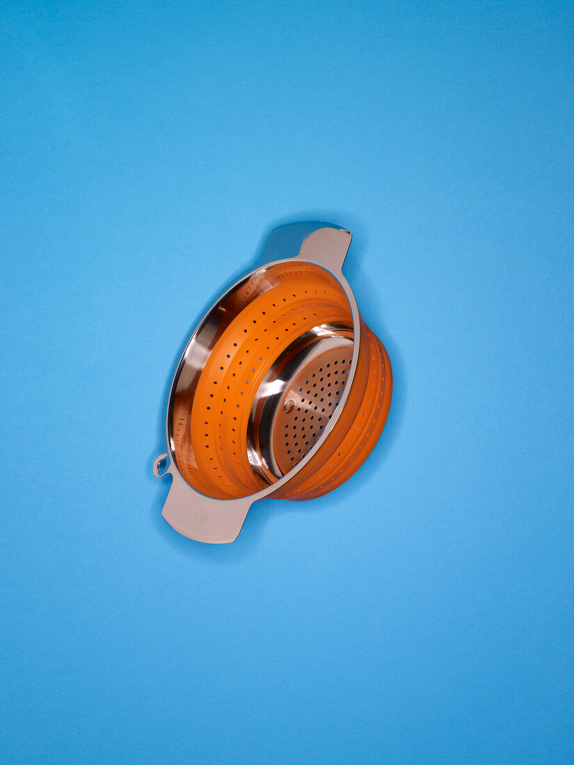 Orange stainless steel colander on blue background