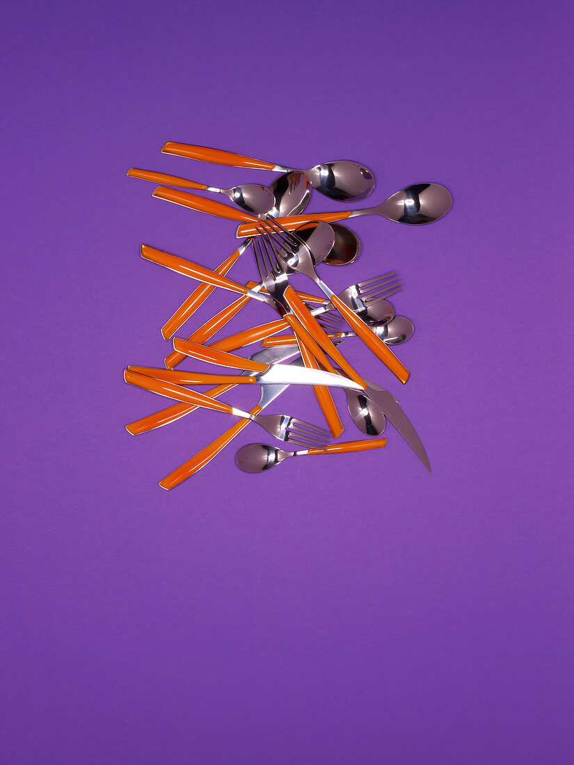 Stainless steel cutlery with red plastic handles on purple background