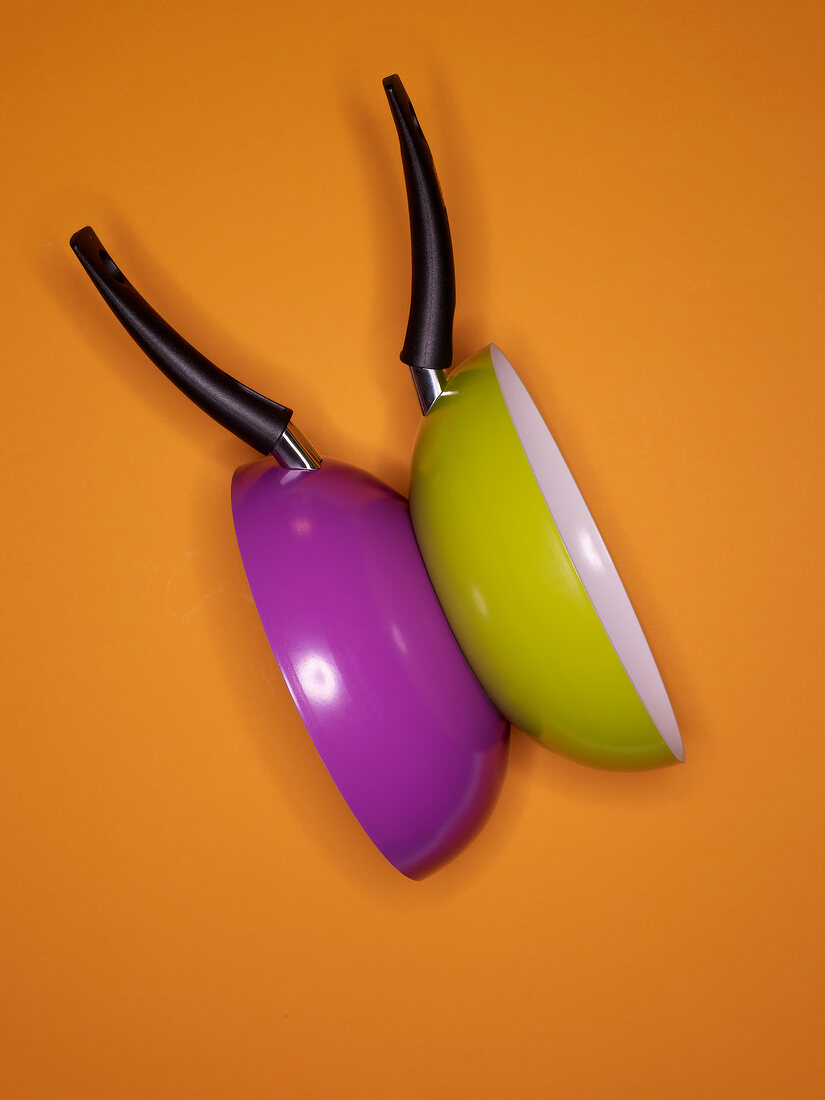 Close-up of two purple and green woks on orange background