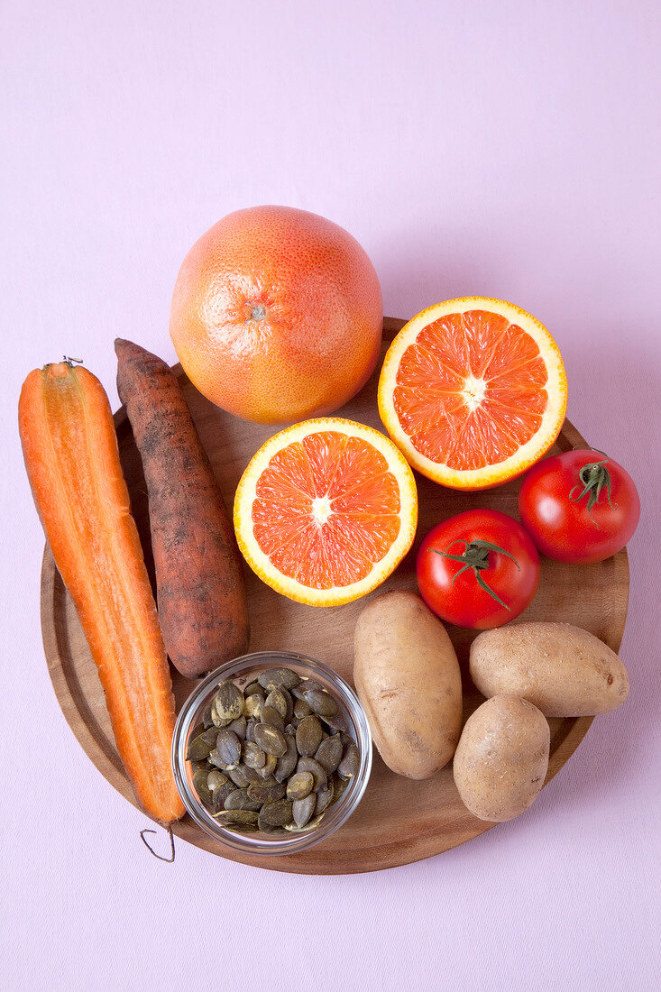 Halved oranges, carrots, tomatoes, potatoes and seeds on pink background