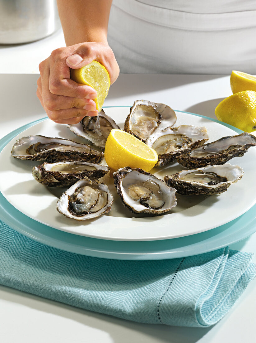 Close-up of hand squeezing lemon on oysters