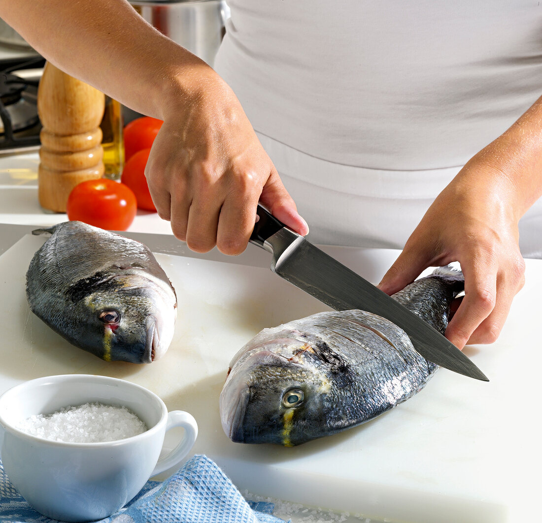 Close-up of hand cutting sea bream on chopping board