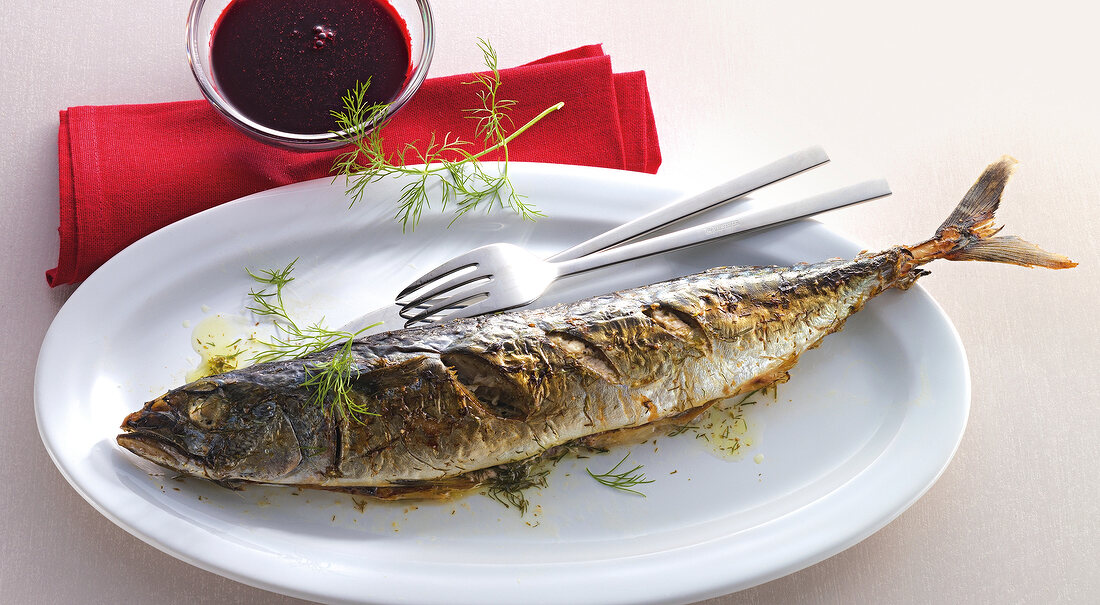 Whole mackerel grilled on plate with berry sauce in bowl