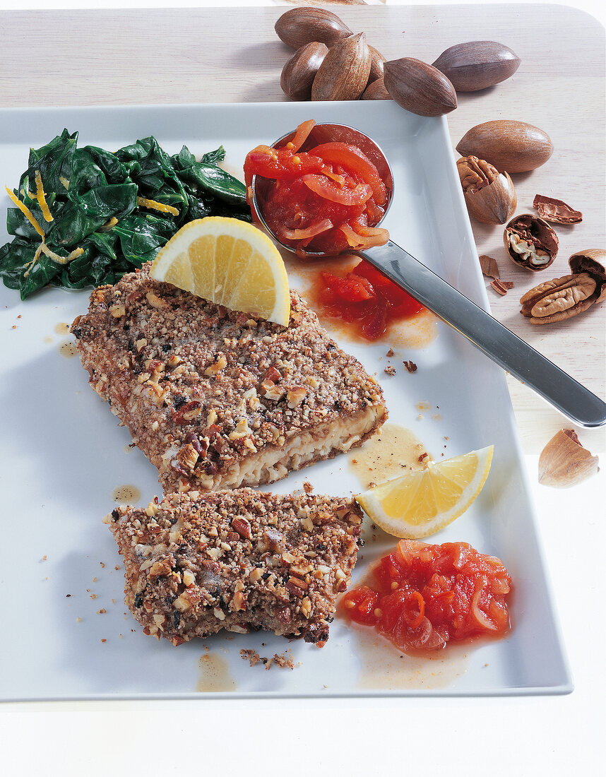 Catfish with nut crust, spinach, tomatoes and lemon in serving dish
