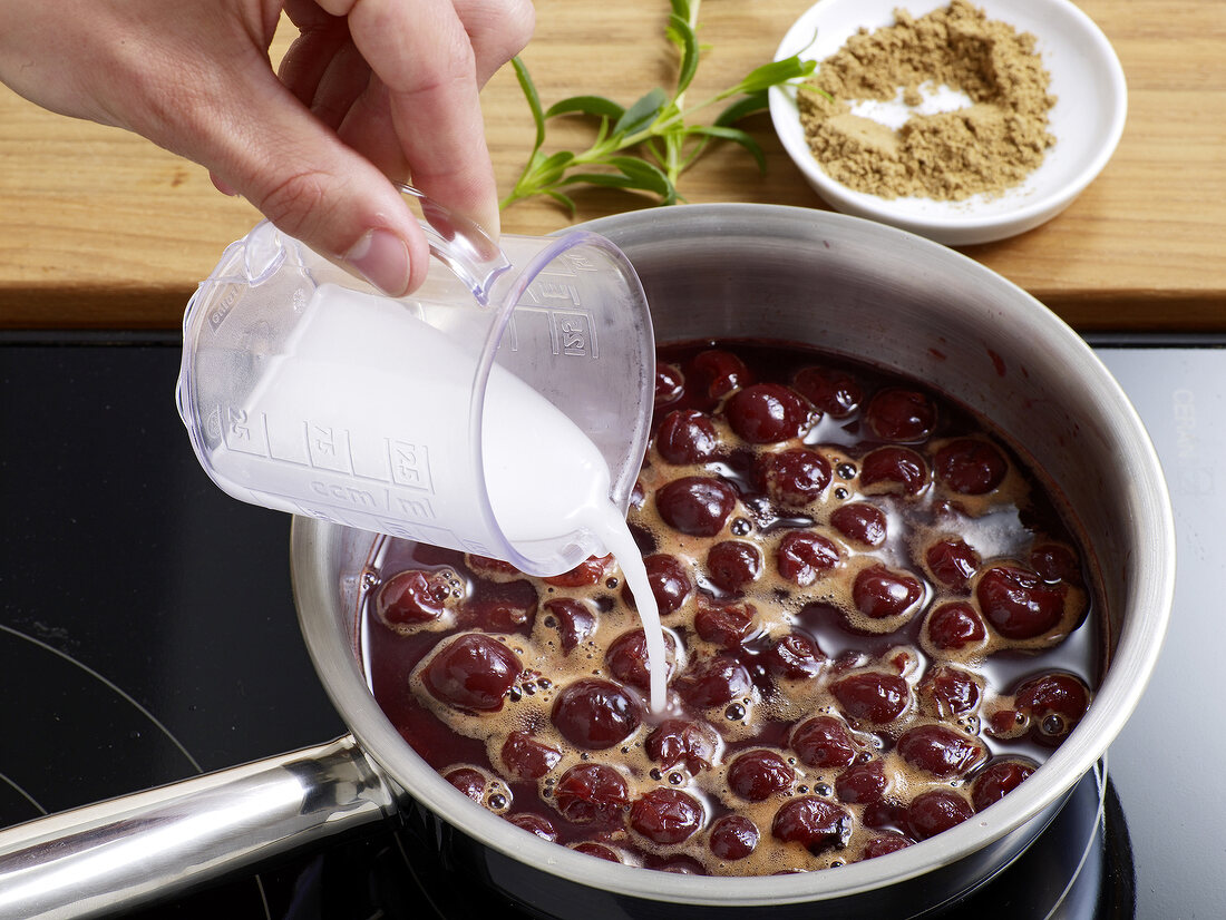 Milk being poured to boiled cherries in sauce pan for preparation of cherry sauce, step 2