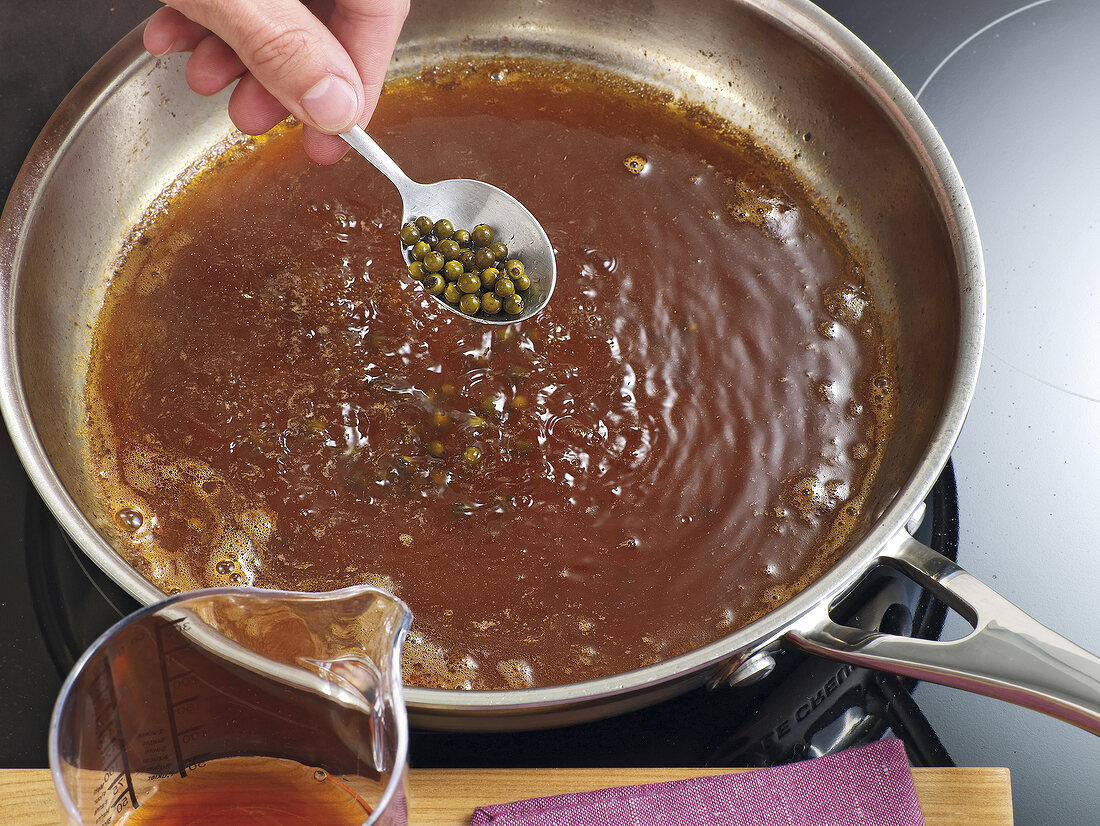 Pepper corns being added to pepper sauce in pan, step 3