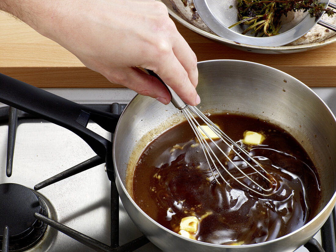 Close-up of hand mixing red wine sauce and butter in sauce pan with whisk, step 5