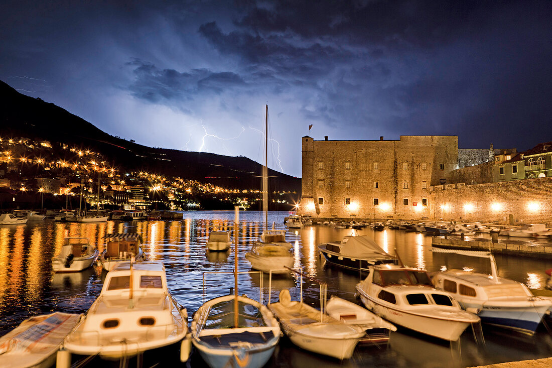 Boats moored on Dubrovnik old harbour with thunderstorm at night in Croatia