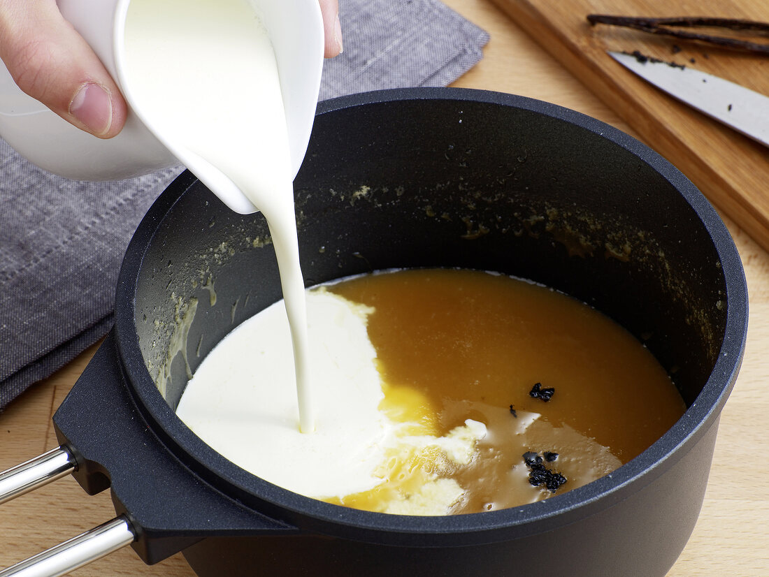 Cream being added in sugar and vanilla liquid for preparation of caramel sauce, step 2