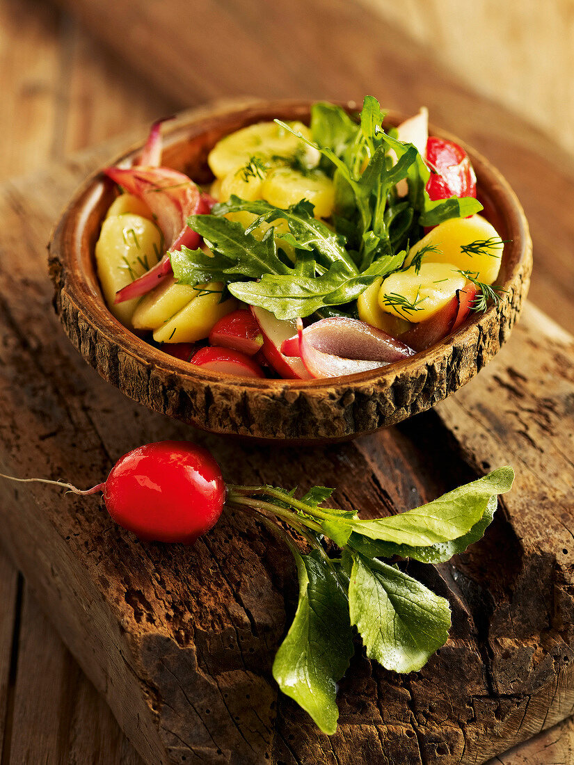 Potato salad with radishes and arugula in wooden bowl