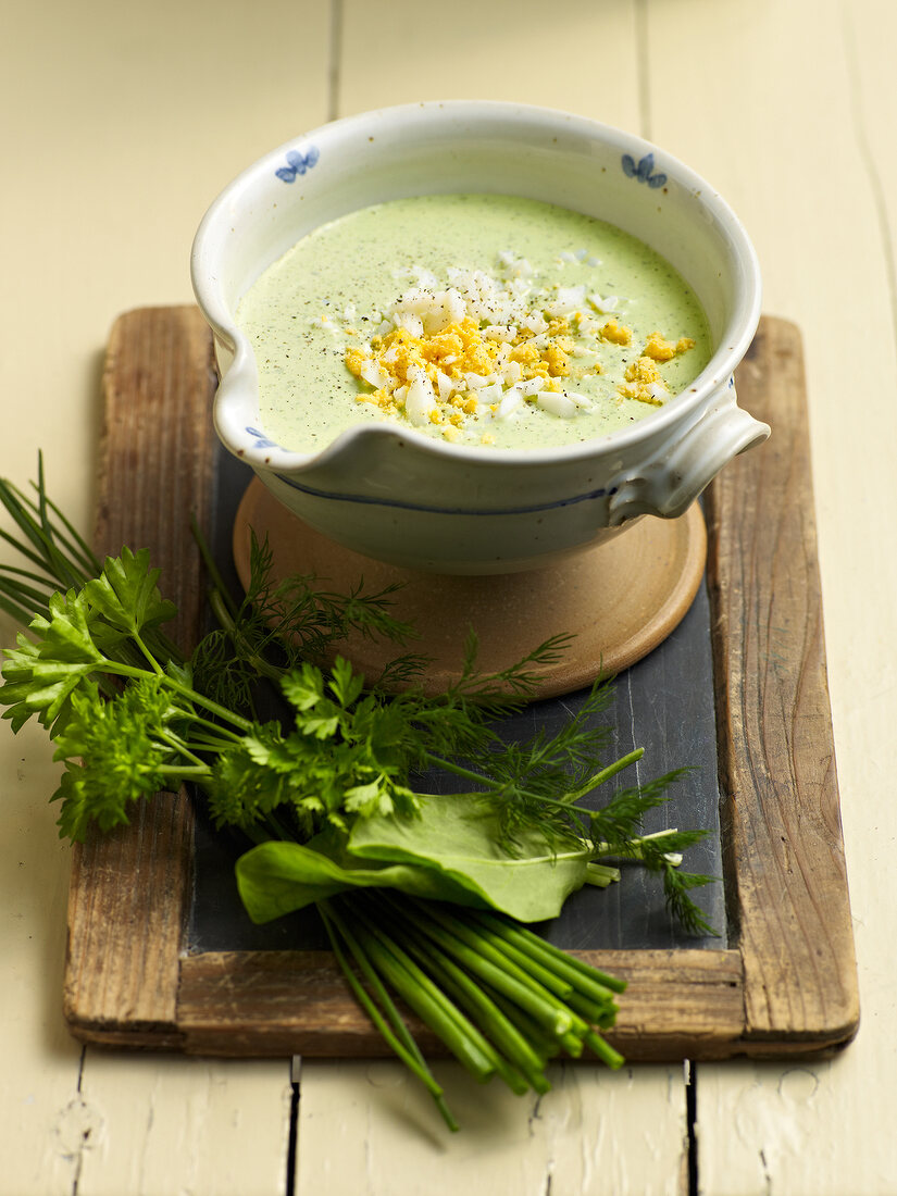 Green sauce in bowl beside fresh herbs on wooden board