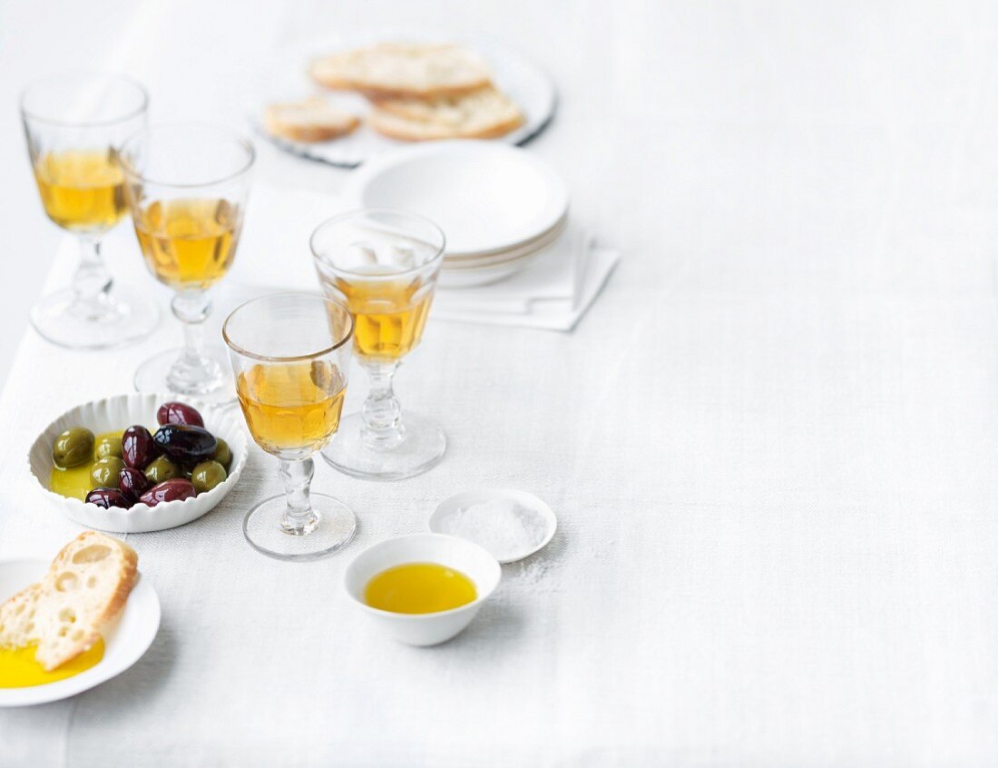 Glasses of sweet wine served with olives, white bread and olive oil on a table