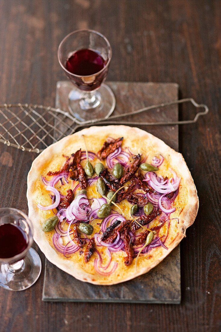 Tarte flambée with red onions, dried tomatoes and caper fruits