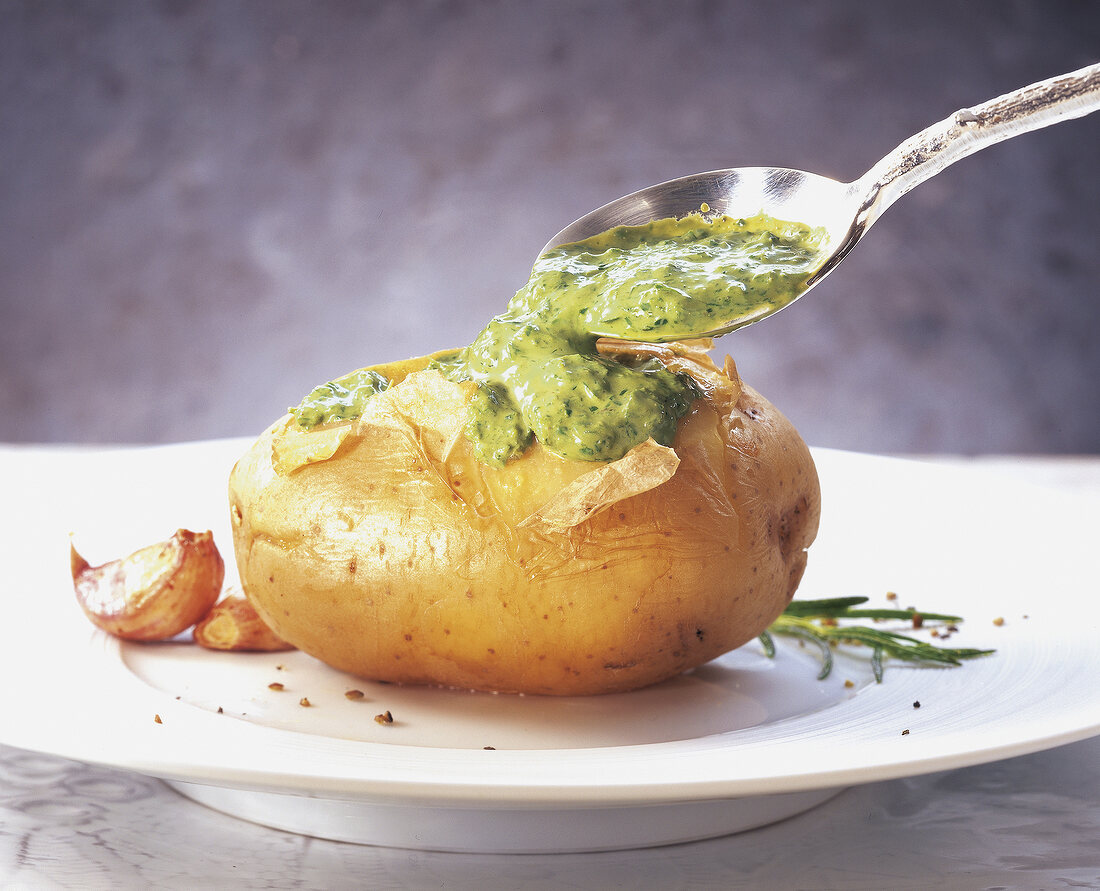 Baked whole potato with green sauce on plate