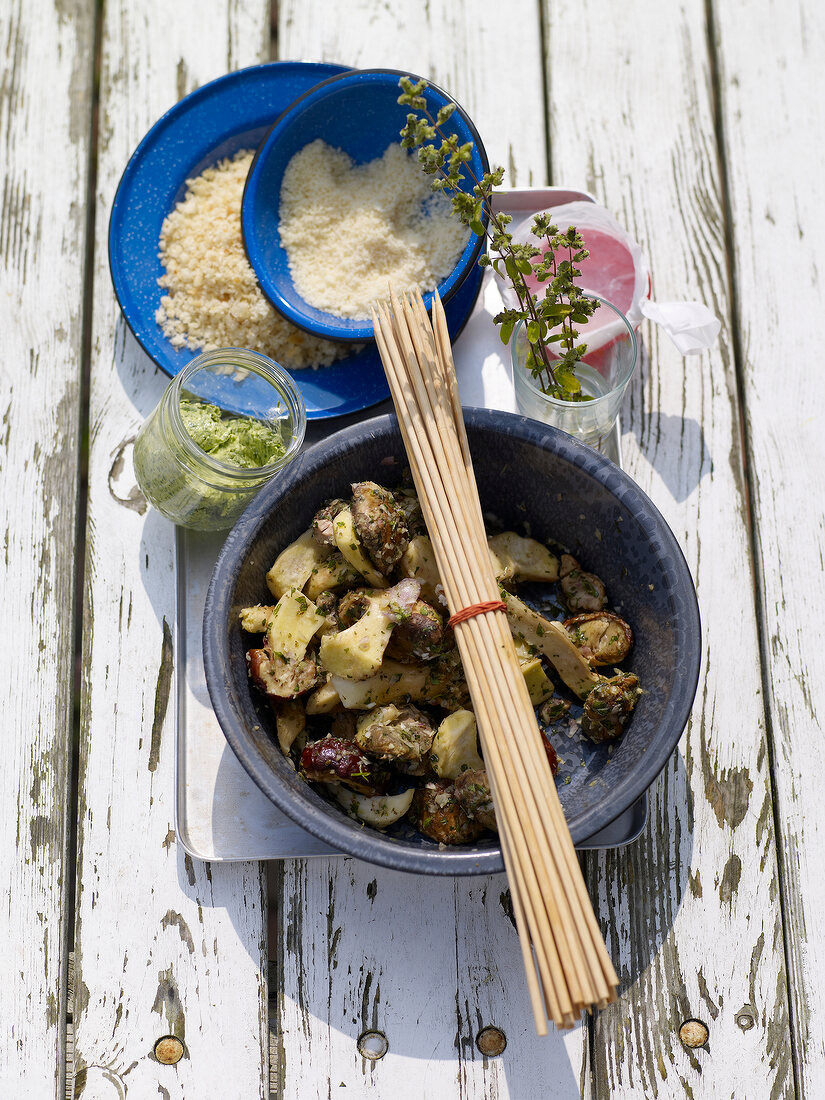 Porcini mushrooms in bowl with herb butter, skewers and bread crumbs on wood