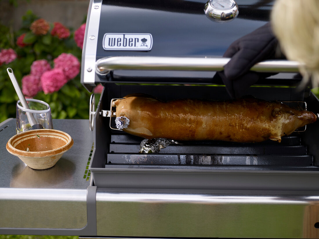 Close-up of suckling pig brushed with oil in charcoal grill