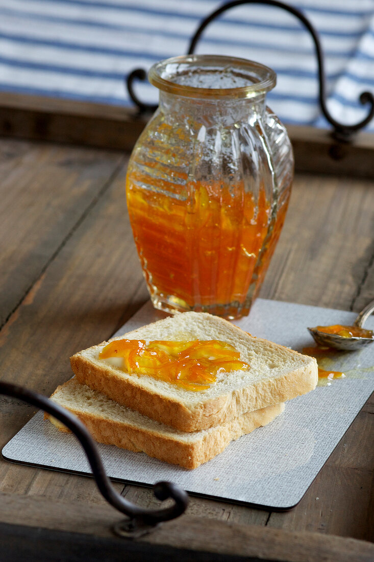 Bitter orange marmalade in jar with bread on wooden tray
